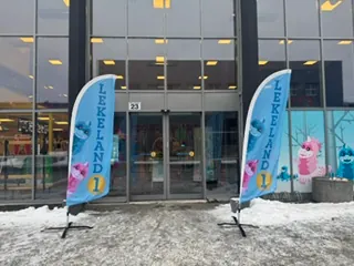 Inngang til Lekeland 1 med reklameflagg og vinterlige omgivelser utenfor bygget.