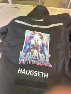 Svart hettegenser med fargerikt trykk og navn på ryggen, produsert med tekstiltrykk.