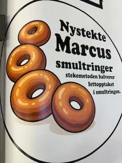 Rund logo med teksten «Nystekte Marcus Smultringer» og illustrasjon av smultringer.