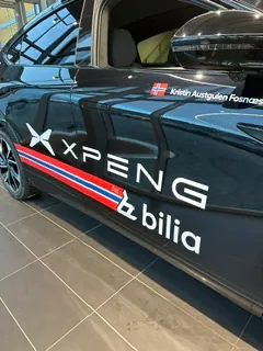 Sort bil med profilering for XXPENG og Bilia, dekorert med norske fargestriper.