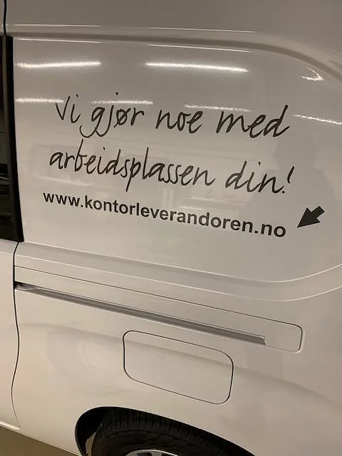 Foliert tekst og nettadresse på sidepanel av varebil for Kontorleverandøren.