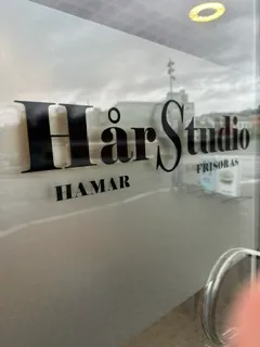 Glassvegg med sort folie og teksten «Hår Studio Hamar» montert i salonglokale.