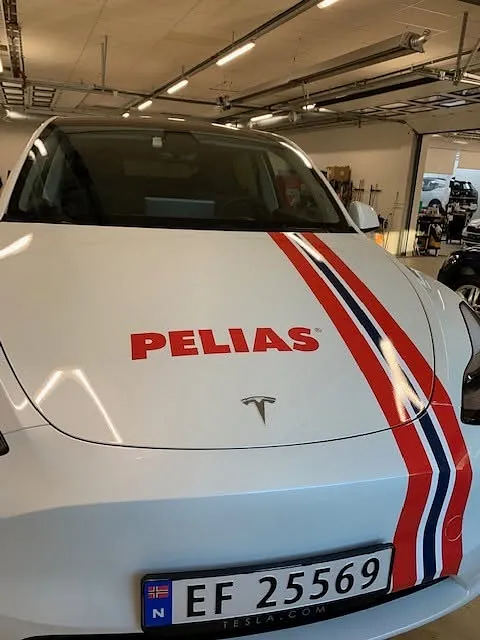 Tesla med Pelias-logo og dekorstriper på panser, klargjort med firmaprofilering.