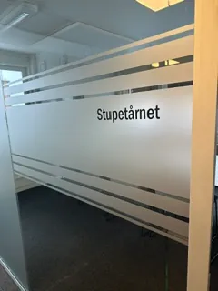Frostet glassvegg med dekorstriper og teksten «Stupetårnet» i kontormiljø.