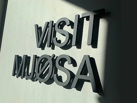 Opphøyde sorte bokstaver med teksten «VISIT MJØSA» montert på lys innendørsvegg.