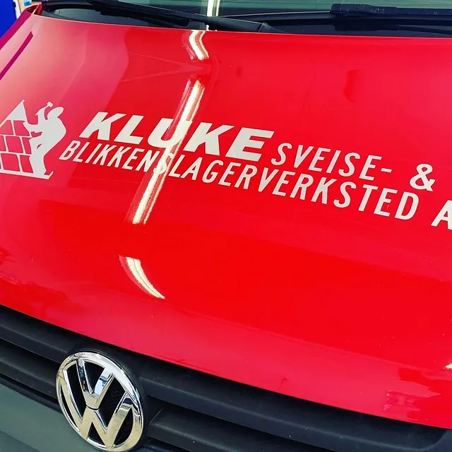 Nærbilde av hvit firmalogo og tekst på panseret til rød Volkswagen varebil.