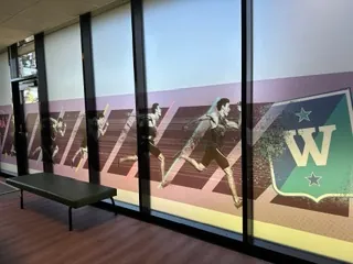 Frostet glassvegg med HamKam-dekor og historiske spillerbilder i kontorlokale.