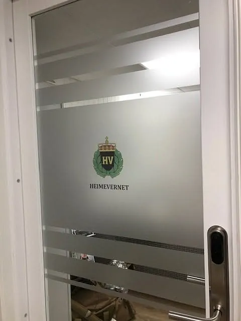 Glassdør med frostet folie og Heimevernets logo montert i kontorlokale.