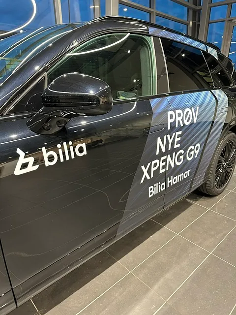 Sort XPENG G9 med kampanjedekor og Bilia-profilering, fotografert innendørs.