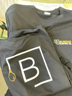 Grå t-skjorter med trykket logo for Bjerkvold Elektro, vist før ferdigstillelse.